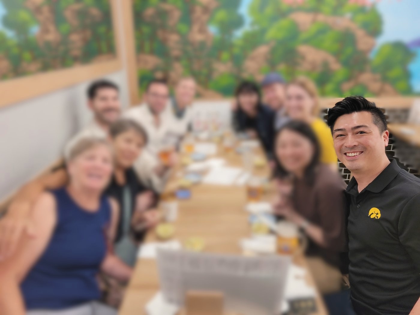 A farewell dinner around a long table at a Tokyo izakaya, guests' faces softly blurred to protect their privacy